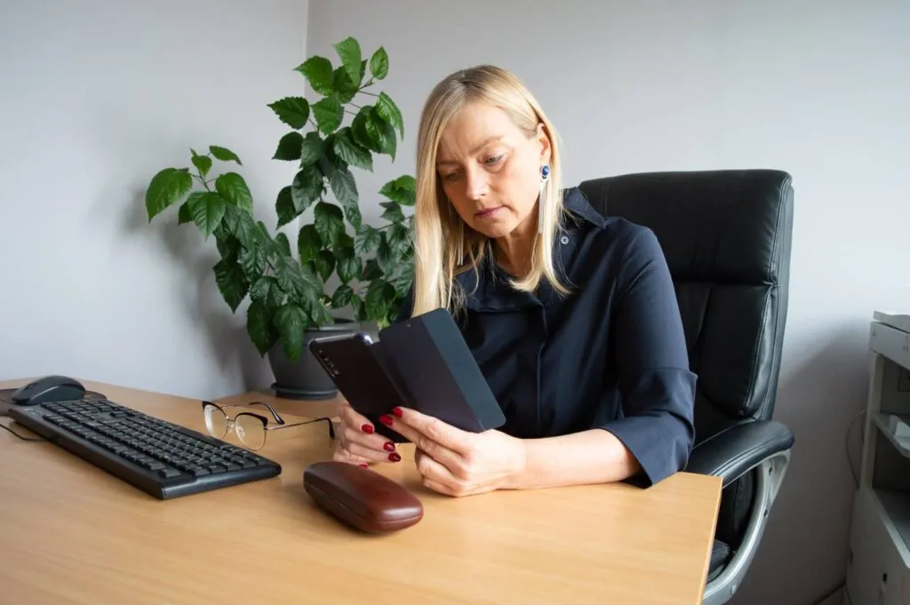 Unternehmerin im Büro blickt auf ihr Mobiltelefon